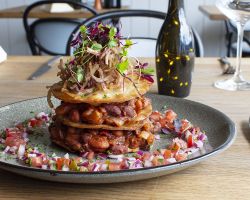 A mixture of beans and vegetables in a rich, smoky tomato sauce, stacked between fried tortillas, served with pico de gallo and fried onions A mixture of beans and vegetables in a rich, smoky tomato sauce, stacked between fried tortillas, served with pico de gallo and fried onions